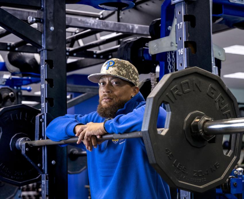 Man wearing a baseball cap leans on free weights in a gym.