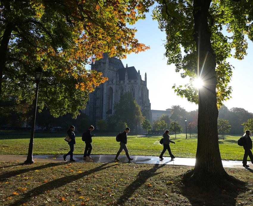 Students walk on the sidewalk of the Cathedral lawn, with Heinz Chapel visible in the background, during the fall.