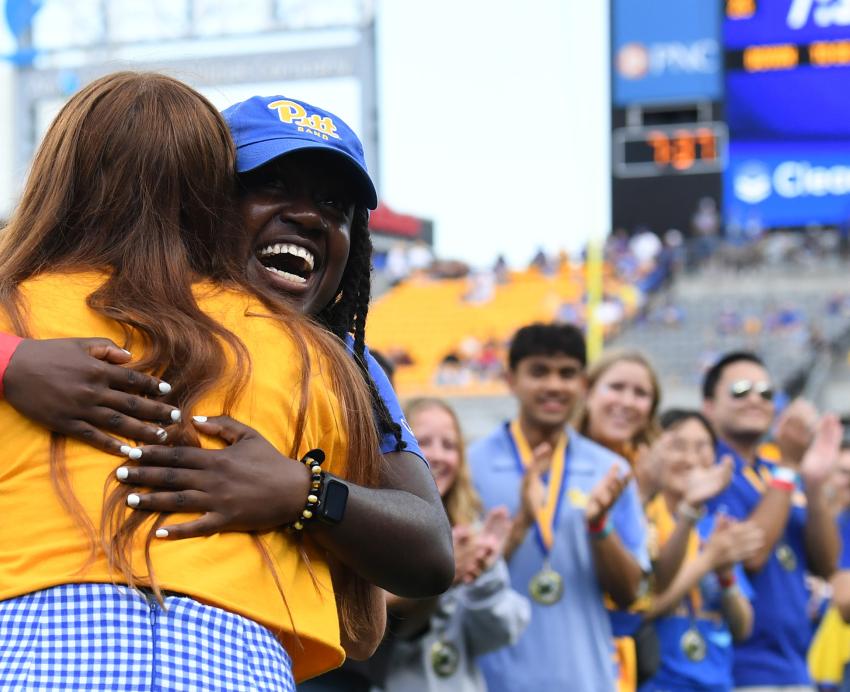 Students embrace on the field of the Acrisure Stadium during a Homecoming Football game.