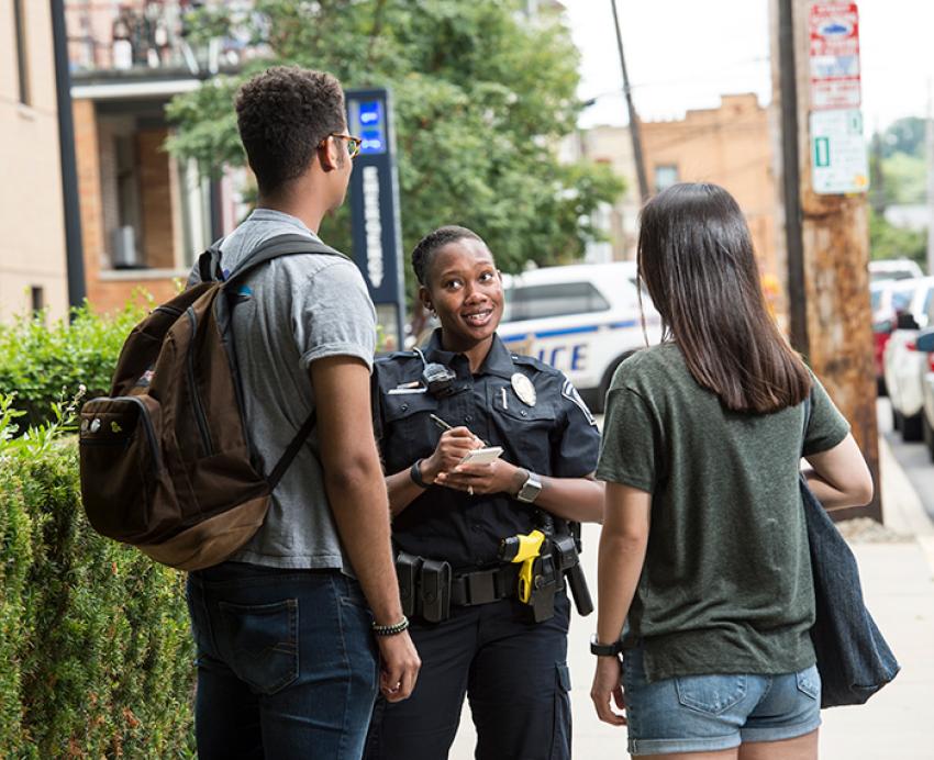 A police officer talks to two students on a sidewalk
