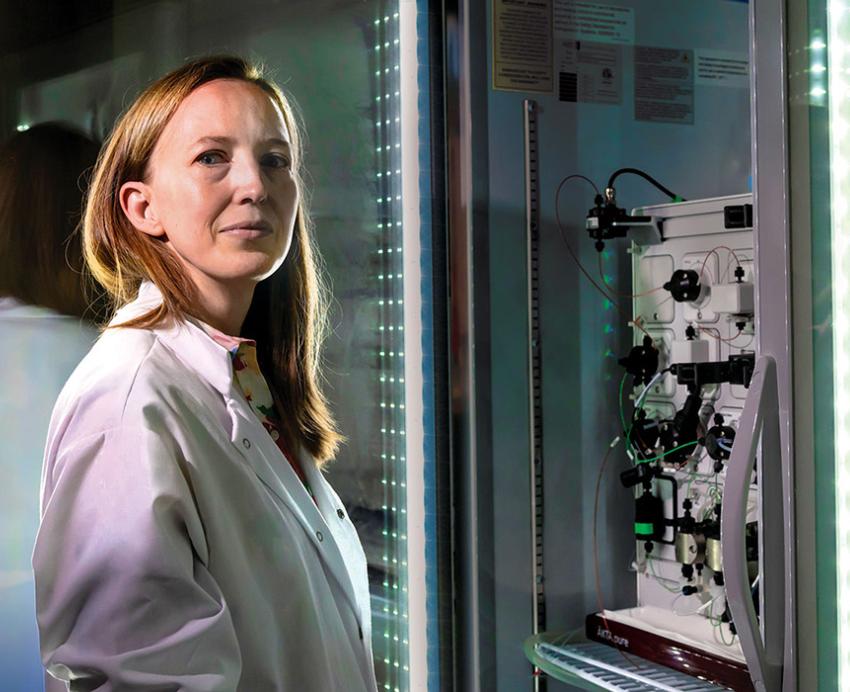 Leah Byrne stands beside a machine and liquid samples in a lab