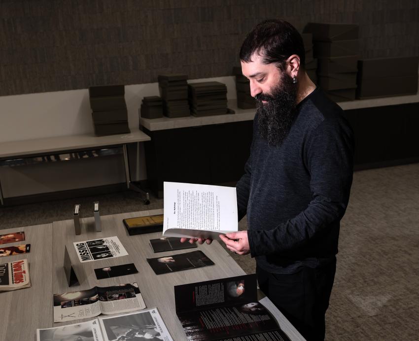 Ben Rubin, Horror Studies Collection Coordinator at the University Library System, stands in a darkly lit room before a table of newly acquired Blair With Project items in the Special Collections section of the Hillman Library. Items include film posters, props, pamphlets and more.