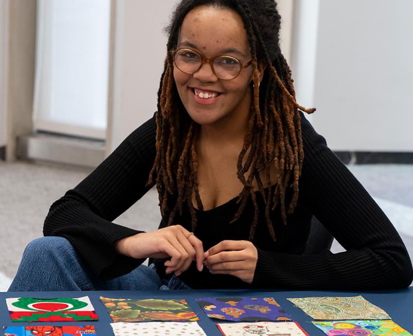 Maria McDill sits at a table where quilt squares are laid out in front of her