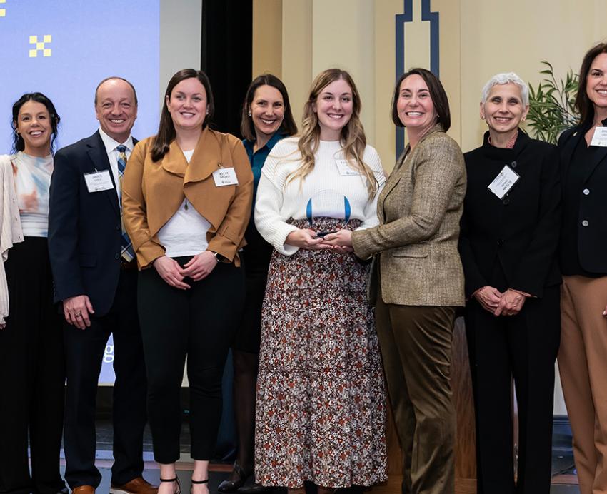 A line of awardees smiles in front of a Pitt-branded screen