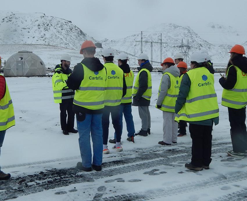 A group of students stand in florescent vests on a snowy plain.
