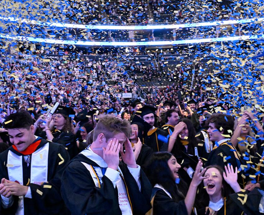 Students at graduation cheering as blue and gold confetti falls
