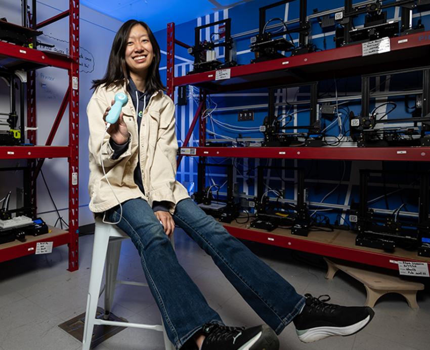 Woman sitting on stool posting for photo in lab holding medical device