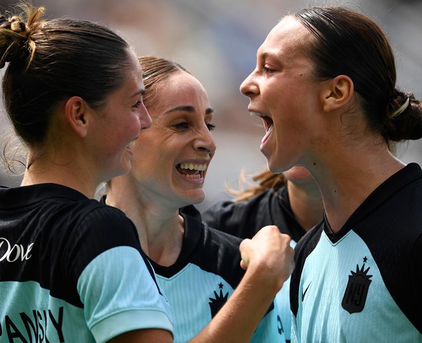 Three soccer players hug and cheer.
