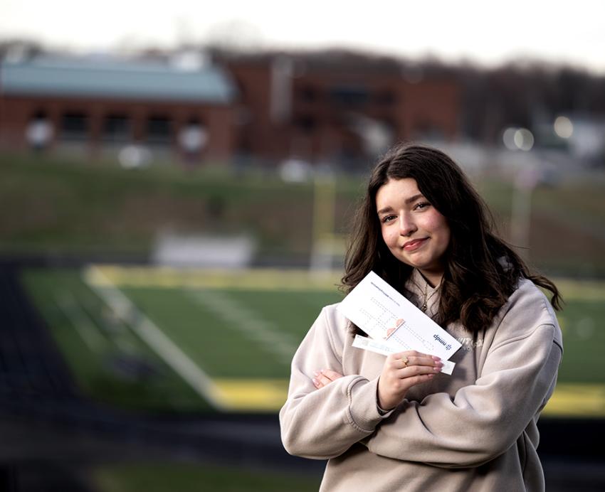 A girl holds a National Marrow Donor Program swab kit while posing for a photo on a school campus