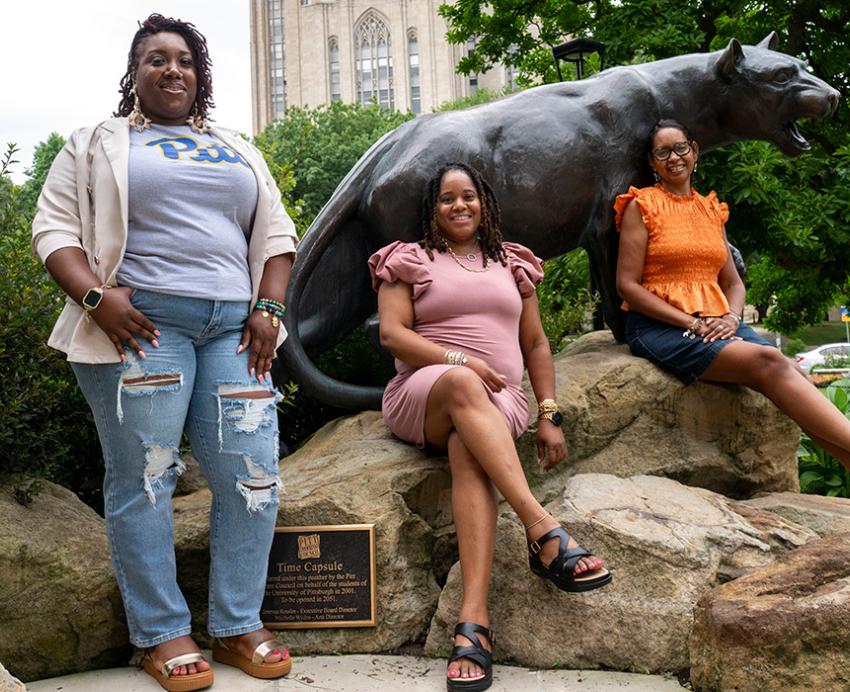 3 students sitting on and around the panther statue