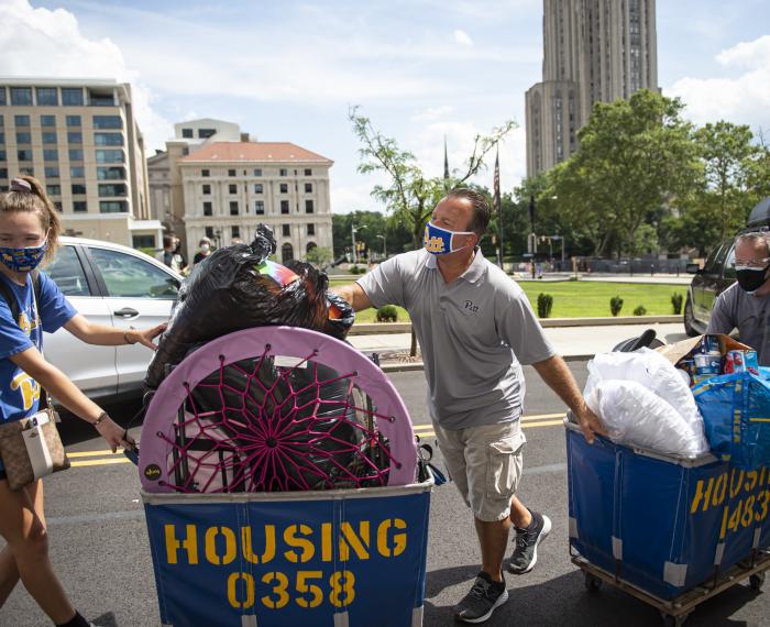 three people dragging blue and gold housing carts through Oakland