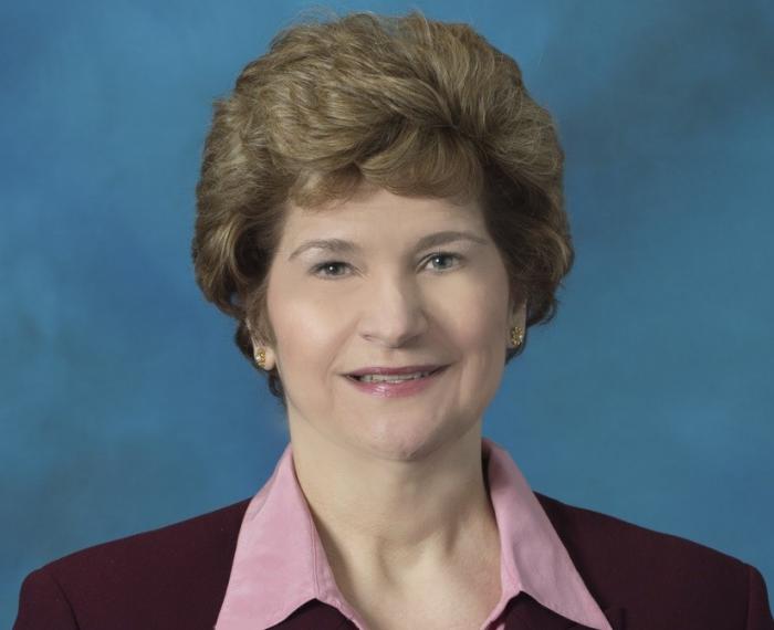 a woman in a pink collared shirt and black blazer in front of a blue photography background