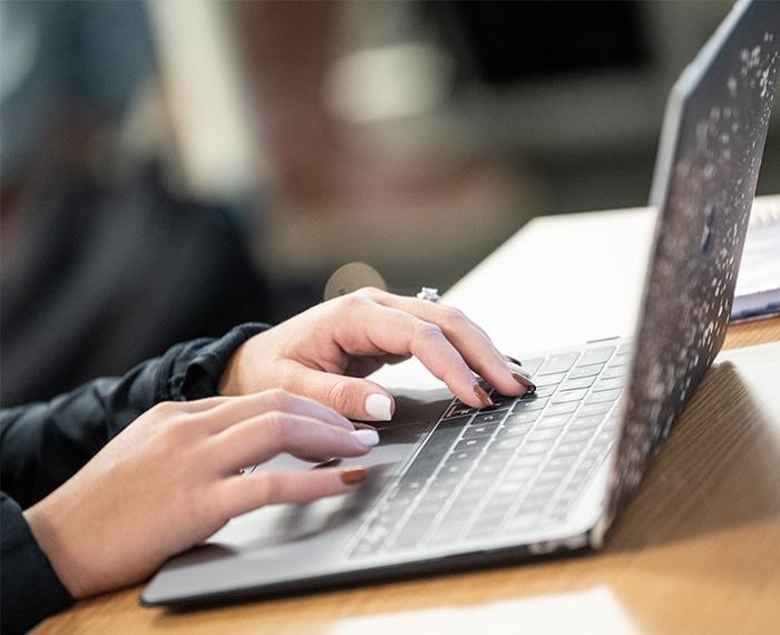Person typing on grey laptop on wooden desk