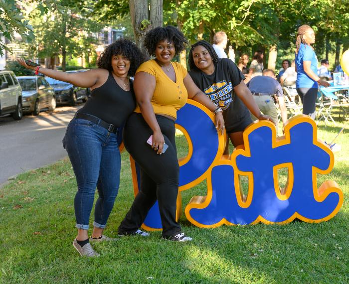 Three students sit on a Pitt display cutout