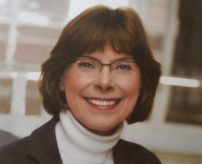 Beth McGrew smiling and wearing white turtleneck and black jacket