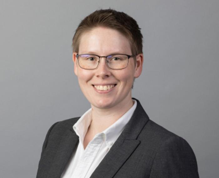 Leslie Marshall in black blazer and glasses in front of gray background