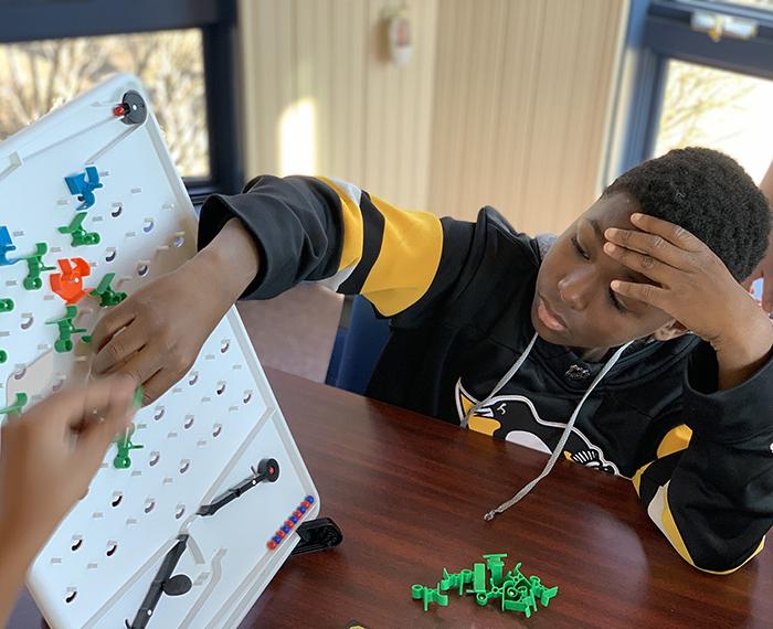 A child in a black and gold sweatshirt reaches for a board on a table