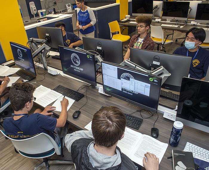 several kids at large computers with books in front of them