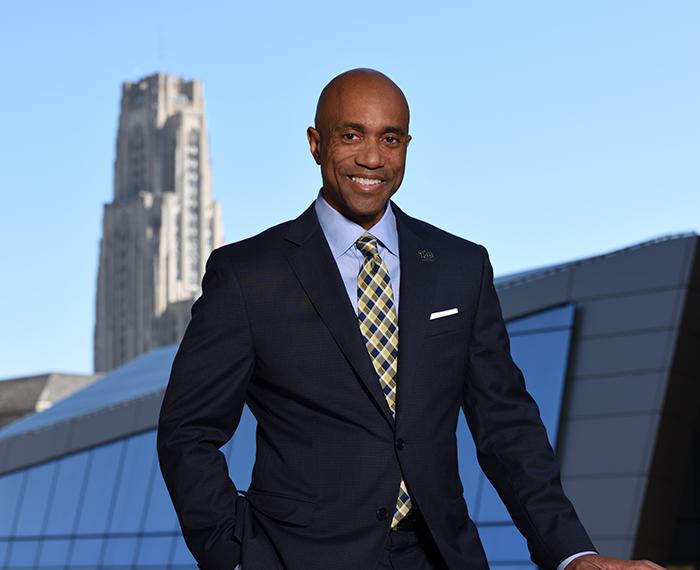 Martin in a suit in front of Benedum Hall with the Cathedral in the background