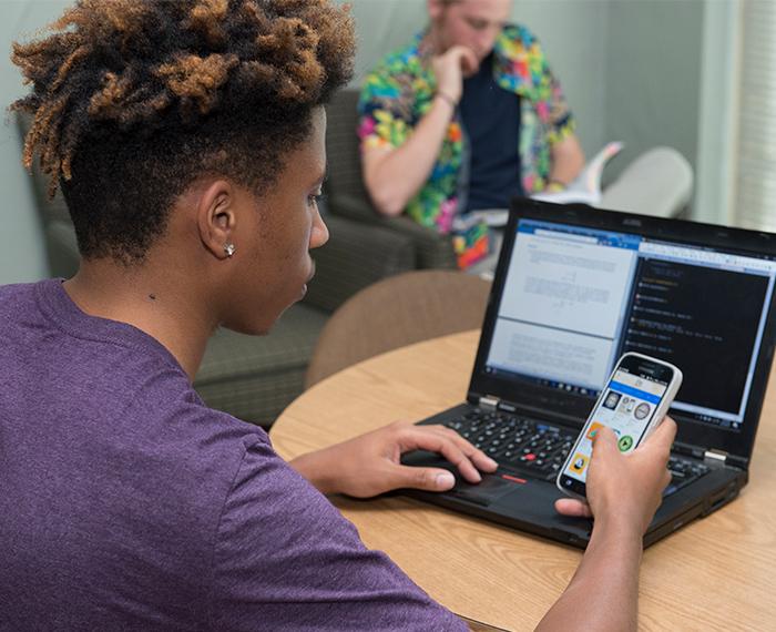 a student at a laptop holding a phone