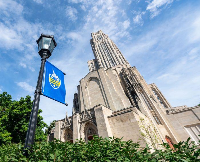 A black street light with a University of Pittsburgh banner sits in the foreground in front of the Cathedral of Learning.