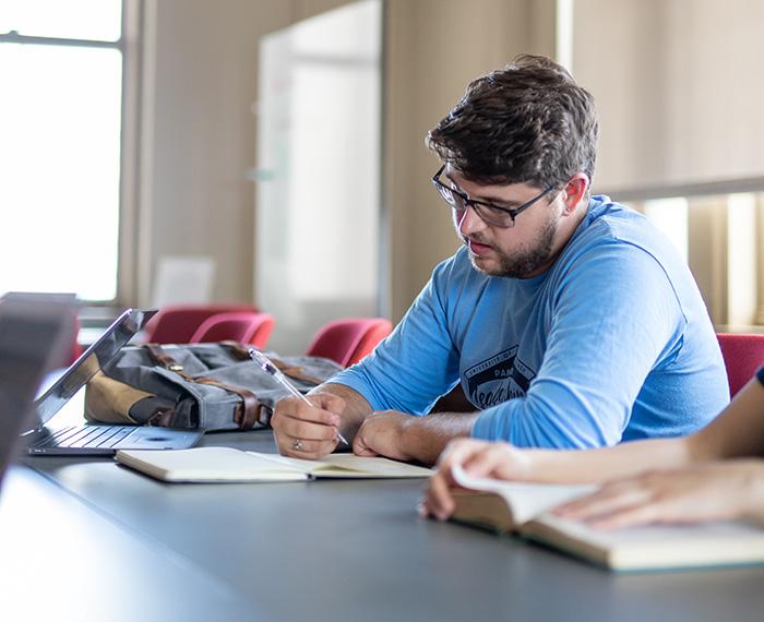 A student in a blue shift writes in a notebook