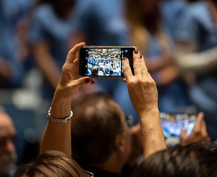 Two hands hold up a phone to take a picture in a crowded room