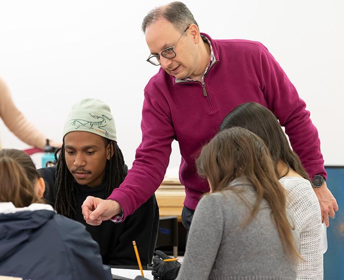 A professor assists a group of students sitting at a table