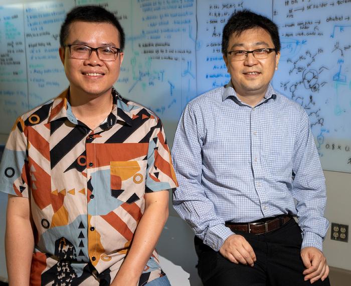 Binh Khanh Mai and Peng Liu sit on a classroom desk in front of a whiteboard