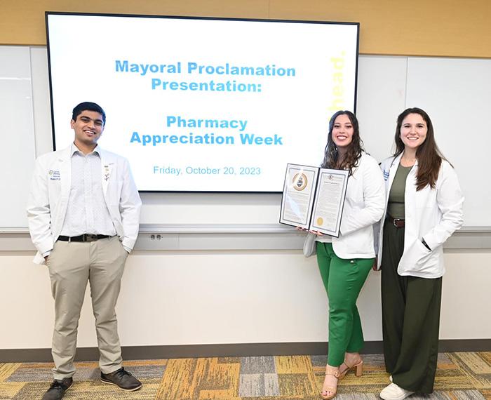 Students hold up the mayoral proclamation while standing beside a presentation screen
