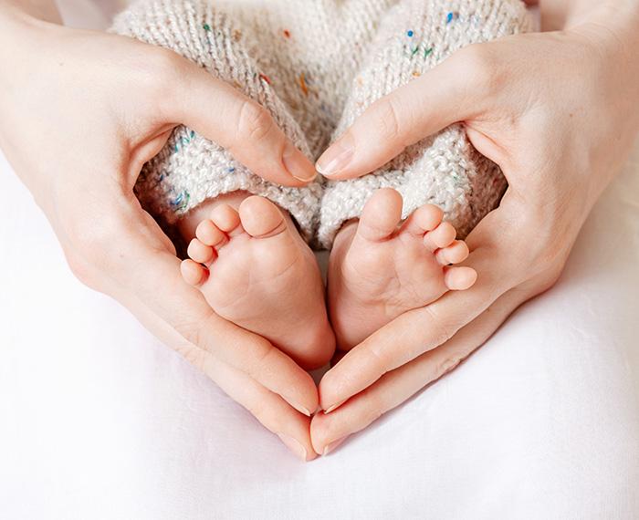 A person makes a heard with hands around a baby's feet