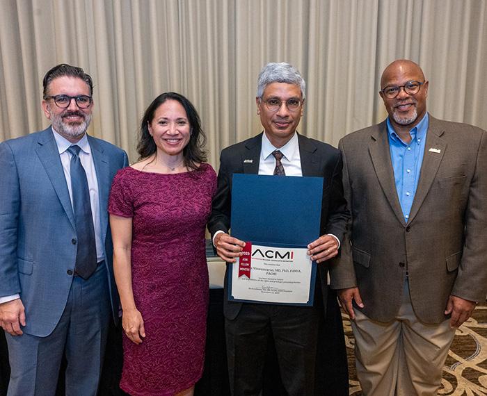 Four people stand in a row. One person, second from the right, holds a certificate