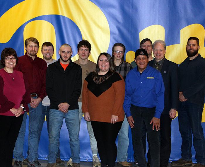 A group of students and faculty stand in front of a Pitt banner
