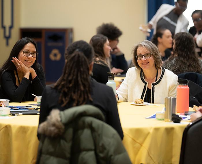 People talk around a table with a yellow tablecloth