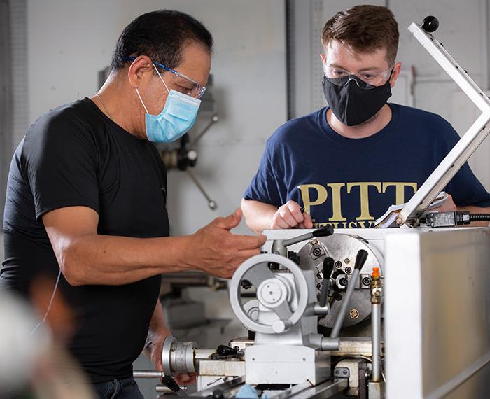 Two people in face masks work on a machine