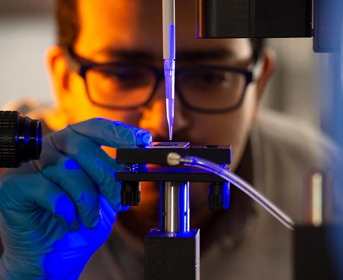 A person adjusts a microscope slide under a pipette device