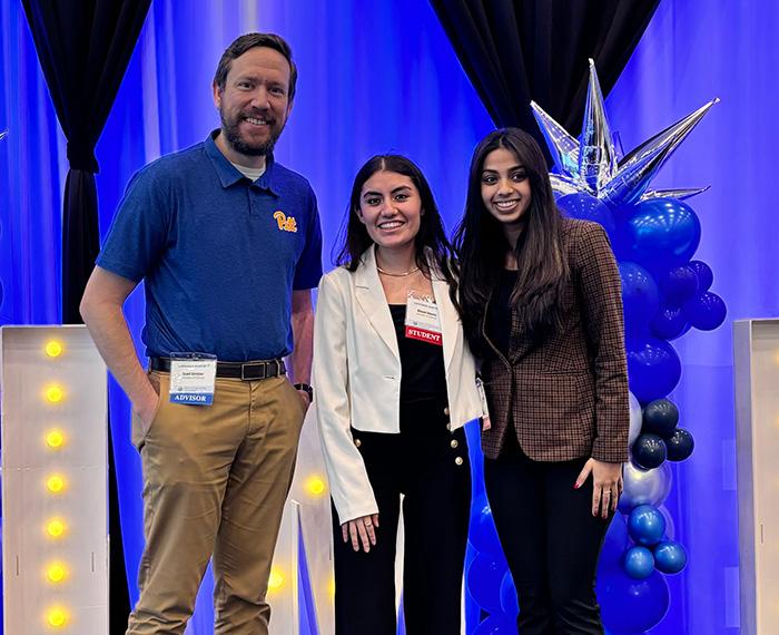 Three people stand in front of a blue background