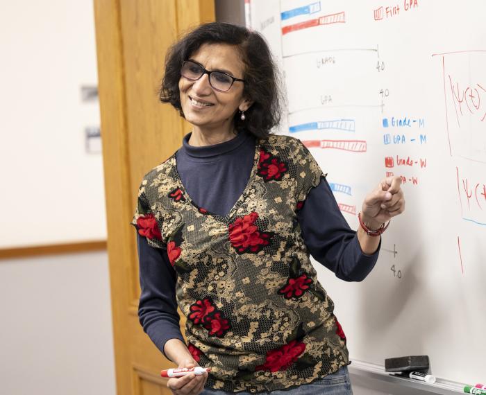 Chandralekha Singh, holding a marker, points at a whiteboard with graphs on it.