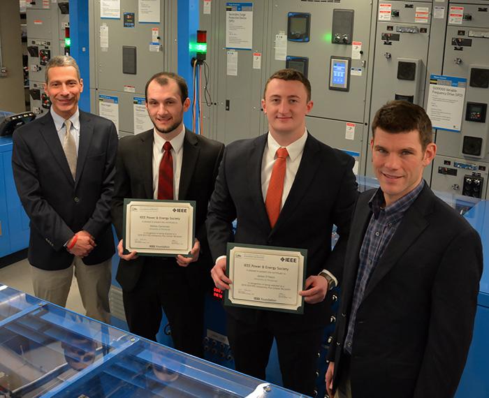Carnovale and Shamus O'Haire hold up certificates beside IEEE representatives