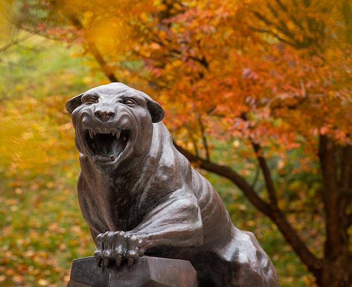 A bronze panther statue against a background of fall leaves