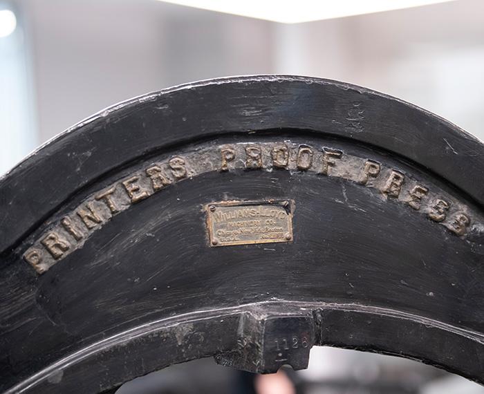 Closeup of hand press with writing reading "PRINTERS PROOF PRESS"
