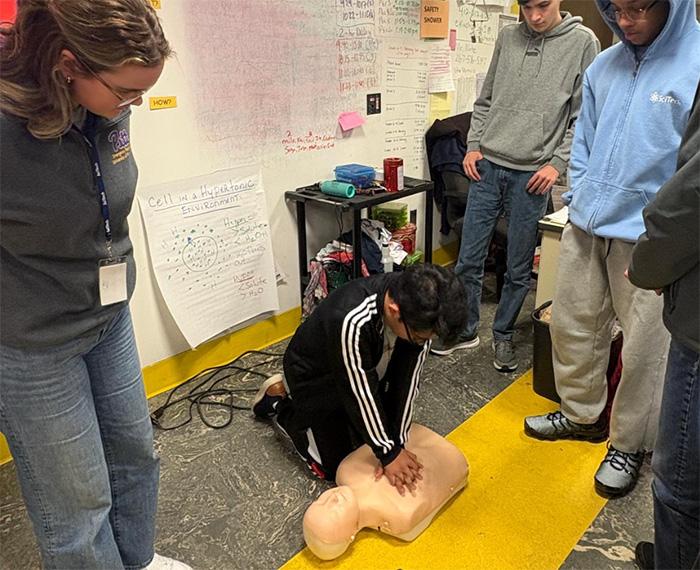 An instructor and students watch as a student practices CPR on a dummy.