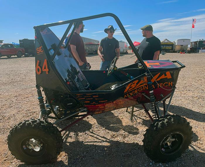 Students stand by a buggy-like car in the desert.