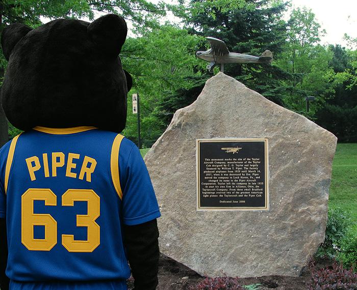 Mascot Piper looks at a stone plaque