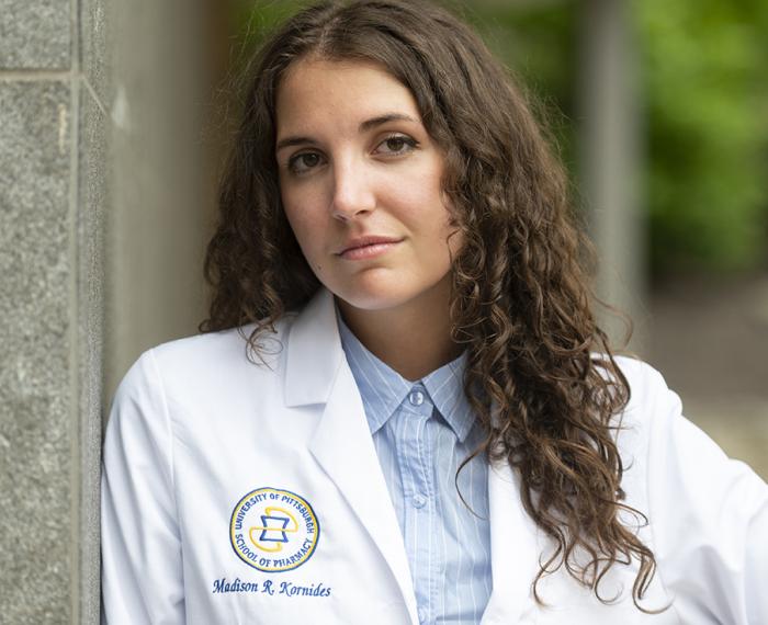 Madison Kornides, in a white lab coat leaning against a stone wall