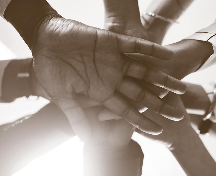 A sepia-tone photograph of 10 hands stacked on top of one another