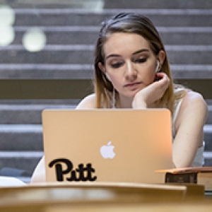 A woman on a laptop with a Pitt sticker