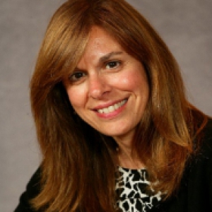 woman with reddish hair in a black sweater and black and white blouse