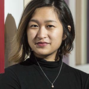 Pearl Galido headshot, wearing black mockneck top and necklace against a background with multi-color stripes