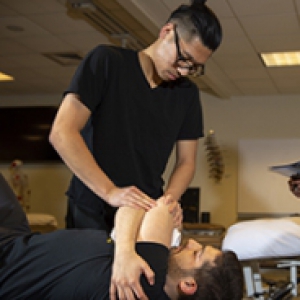 A physical therapy student performs tests on a patient, while a professor observes
